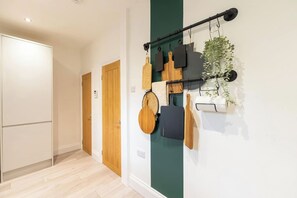 Un couloir avec un étagère fixée au mur, sur laquelle sont rangés des ustensiles de cuisine, une plante en pot et une porte blanche.