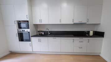 Una cocina con armarios blancos, microondas, horno y encimera negra.
