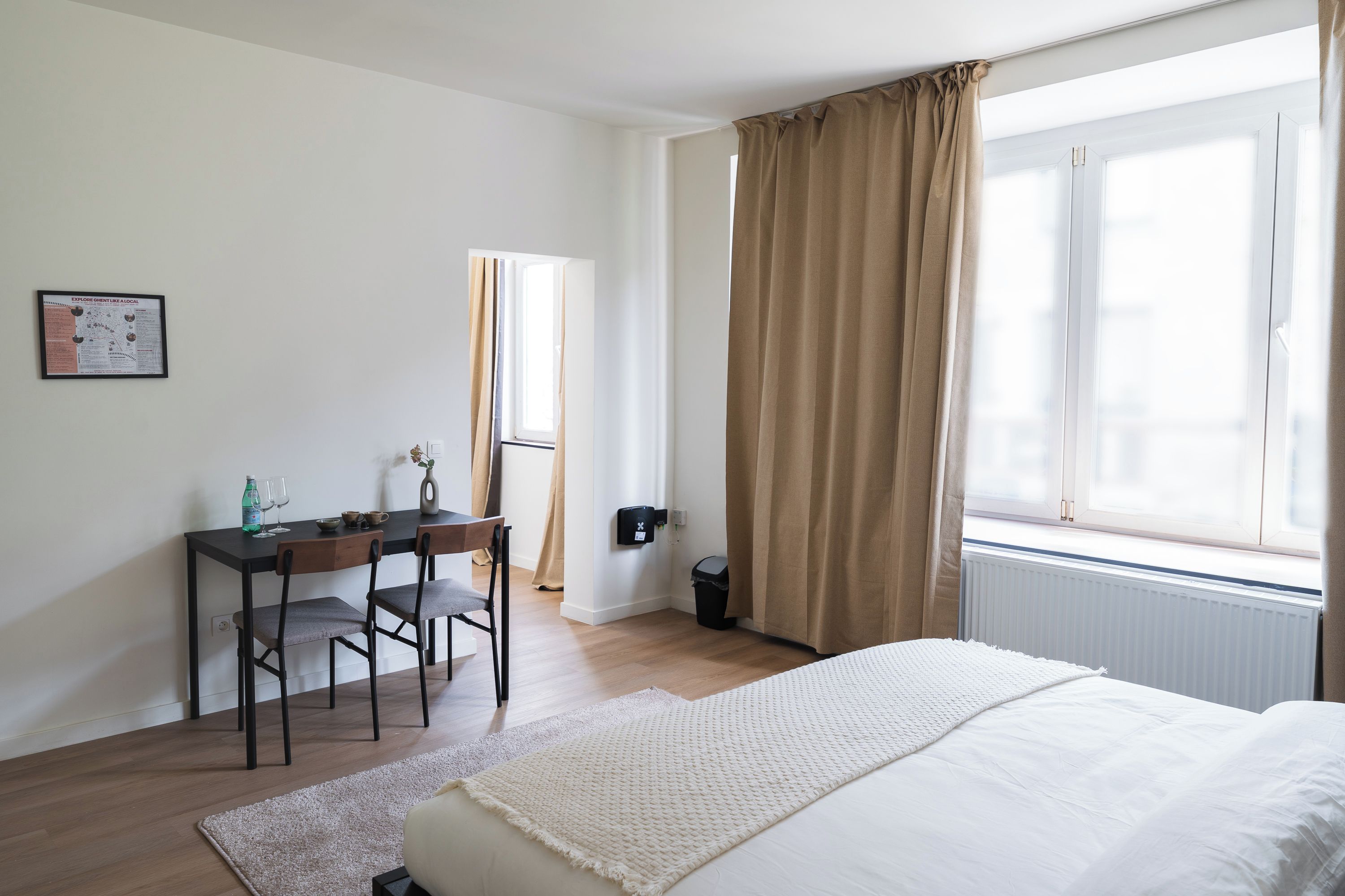 A bedroom with a bed, a desk, and a window with curtains.