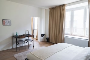 Un dormitorio con cama, escritorio y ventana con cortinas.