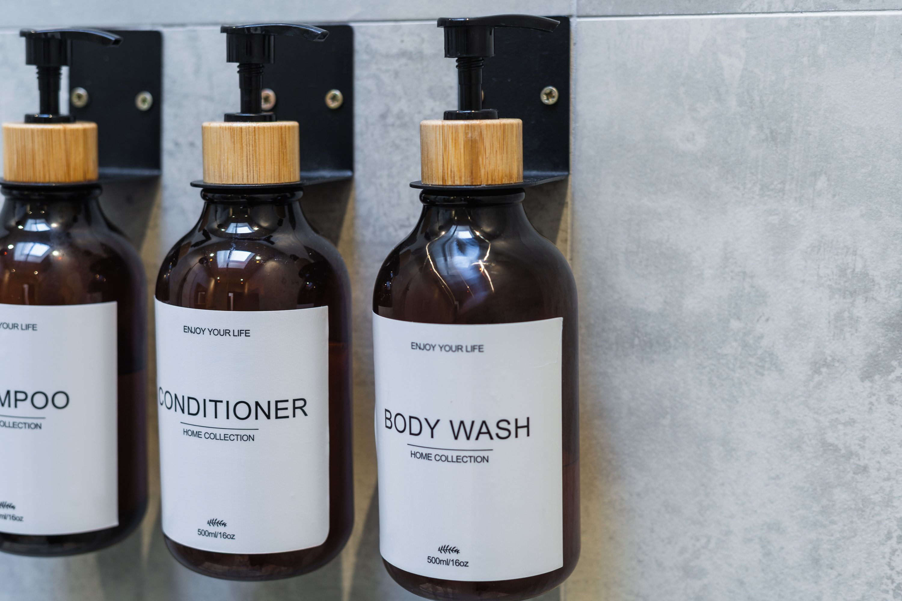 Three bottles of shampoo, conditioner, and body wash on a wall.