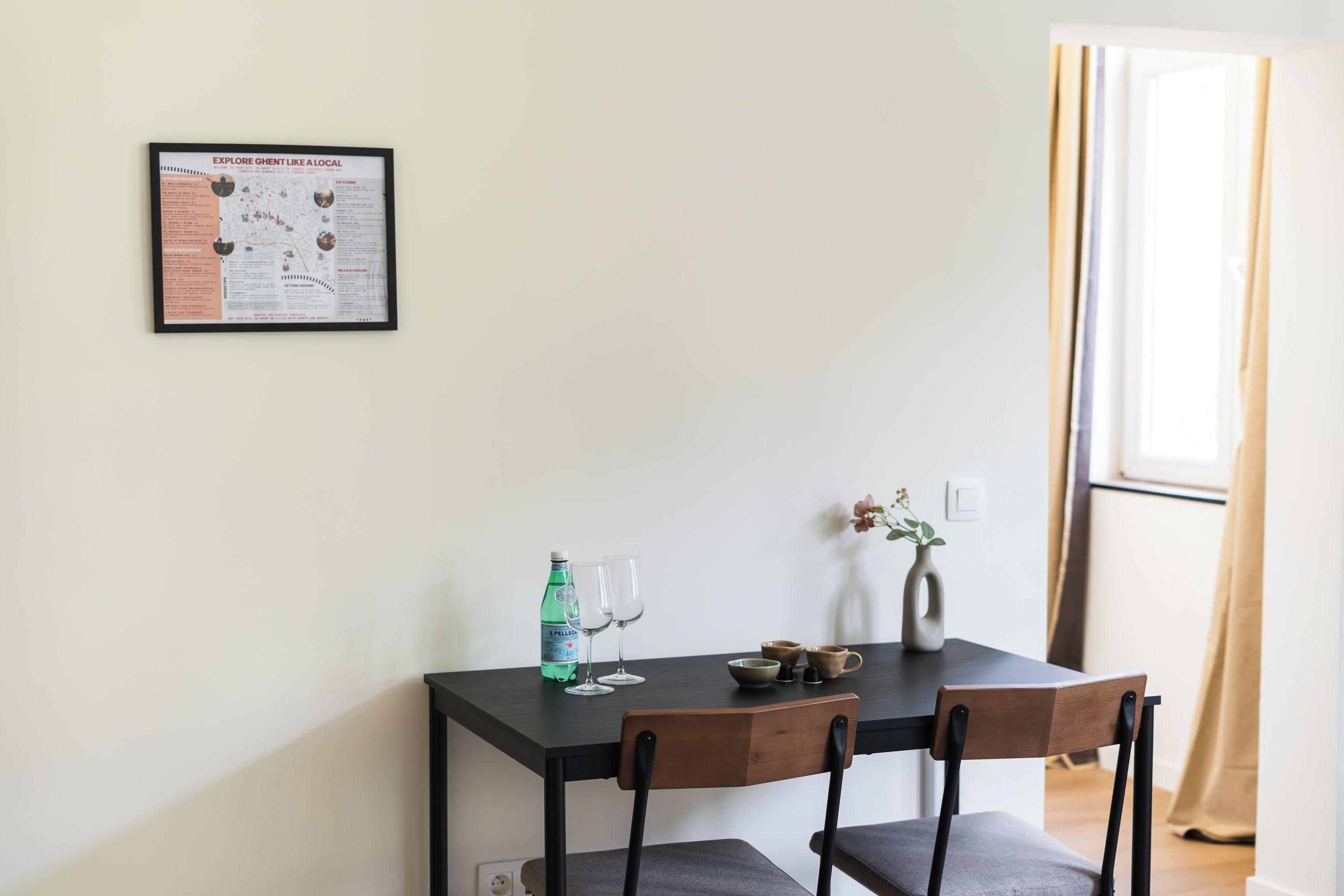 A dining table with chairs, a framed map, a bottle, and glasses.
