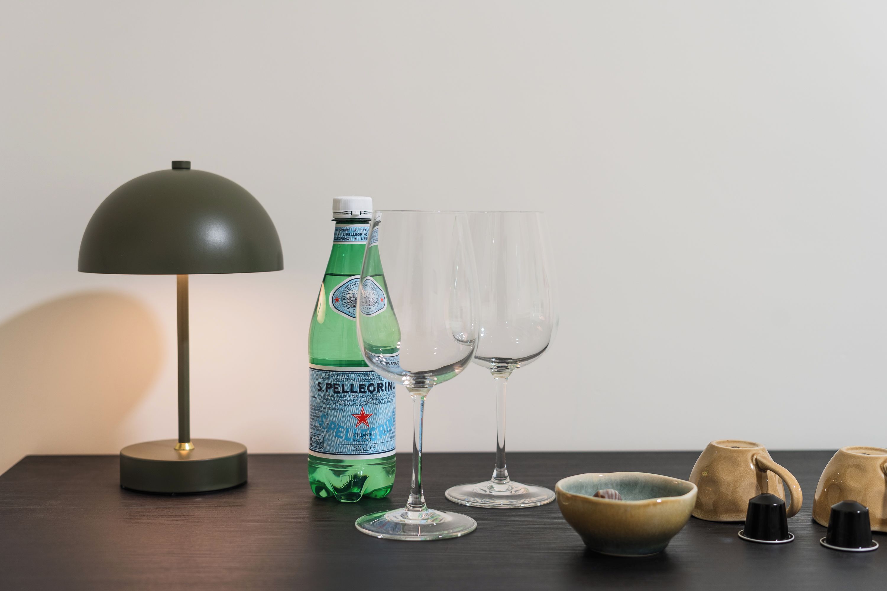 A table with a green bottle, two glasses, a lamp, a bowl, and two teapots.