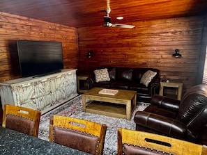 A cozy living room with a wooden ceiling, a flat-screen TV, leather sofas, a coffee table, and a patterned rug. - Cozy 2-bedroom cabin style apartment in the peaceful Fayetteville area. (Elkins)