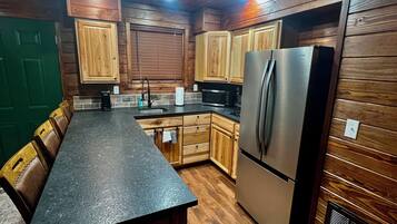 A kitchen with wooden cabinets, a stainless steel refrigerator, a black countertop, and a green door.