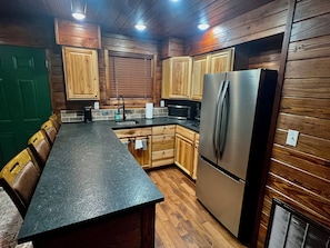 A kitchen with wooden cabinets, a stainless steel refrigerator, a black countertop, and a green door. - Cozy 2-bedroom cabin style apartment in the peaceful Fayetteville area. (Elkins)