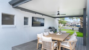 An outdoor patio with a wooden table and wicker chairs, a ceiling fan, and a view of a residential street. - Mercator Waters - Relax, Unwind & Play (Saint Huberts Island)
