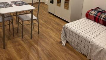 Een kamer met een eettafel, stoelen, een garderobe en een bed met een geruit plaid.