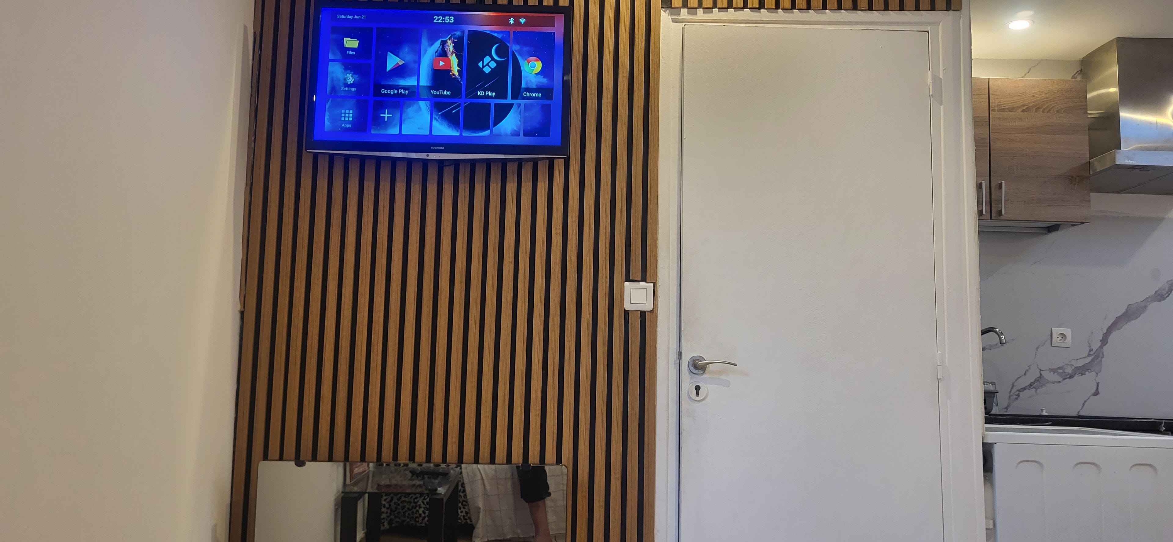 A flat-screen TV mounted on a wooden wall above a white door, displaying a digital interface with various app icons.