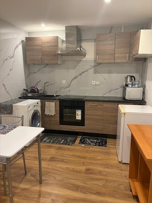 A compact kitchen with a washing machine, oven, microwave, and a small refrigerator. - Vrbo Property (Lille)