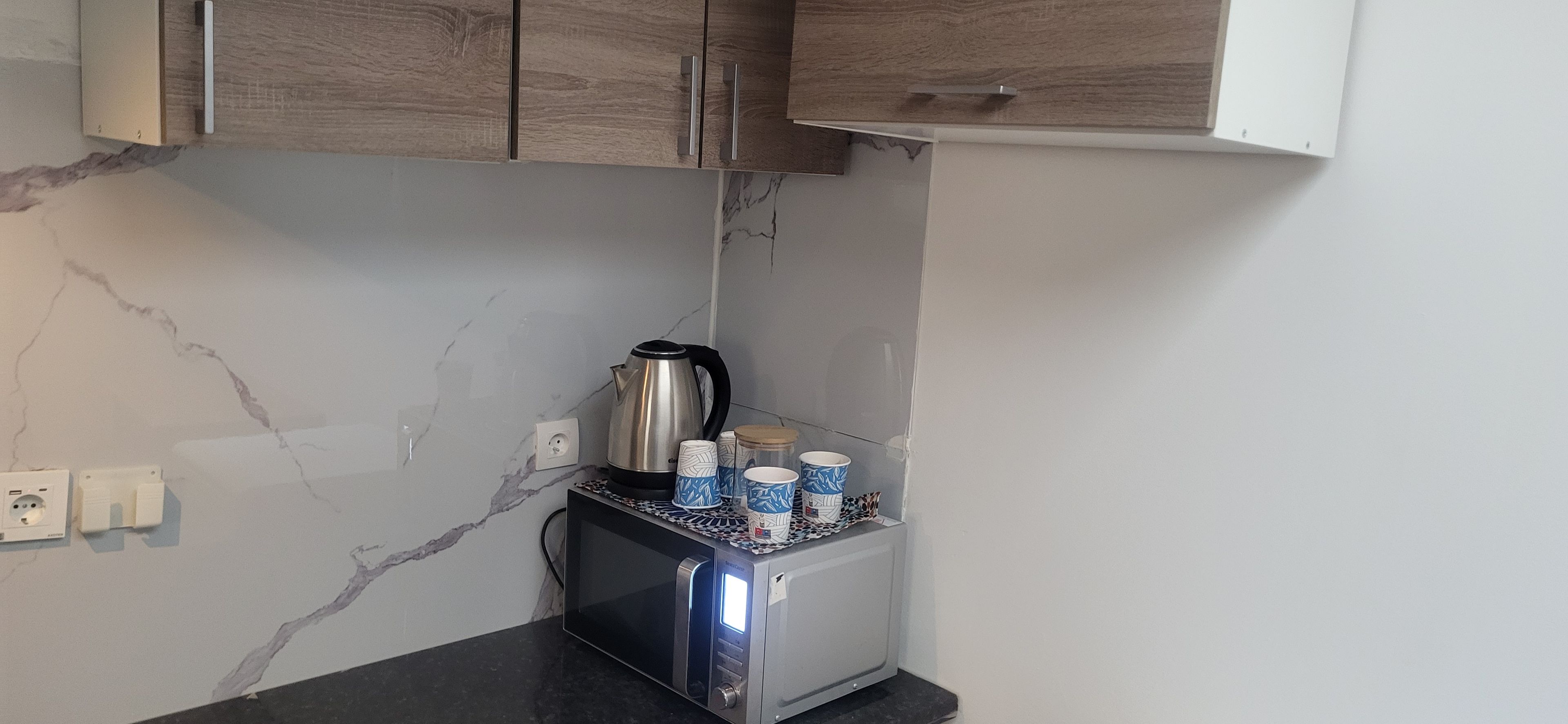 Een kitchenette met een magnetron, waterkoker en kopjes op het aanrecht.