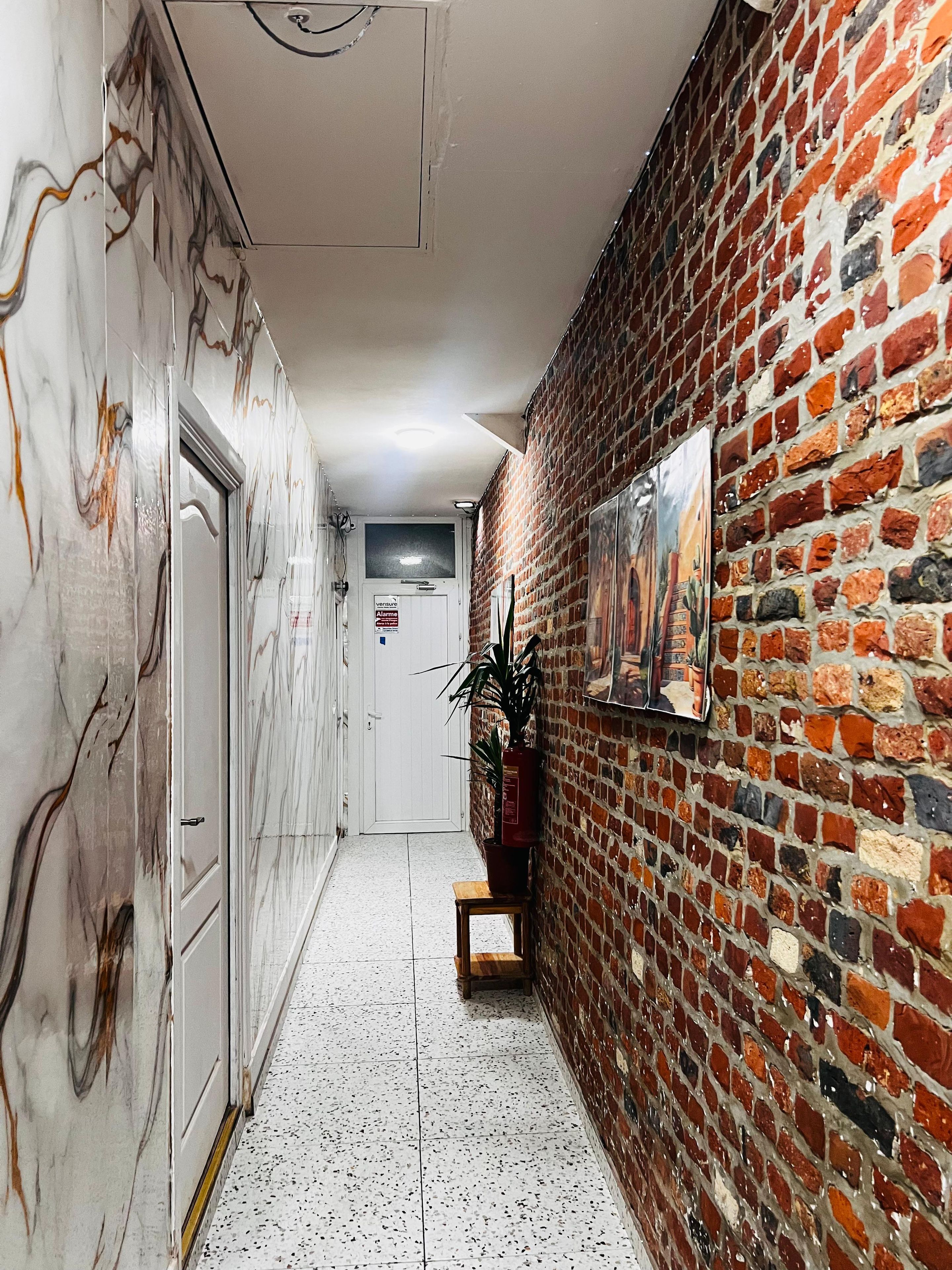Een gang met aan de ene kant een marmeren wand en aan de andere kant een bakstenen wand, die leidt naar een deur aan het einde.