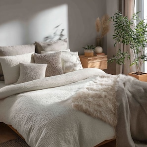 A bedroom with a bed, pillows, a blanket, a wooden nightstand, a potted plant, and a window with curtains. - Vrbo Property (Lille)