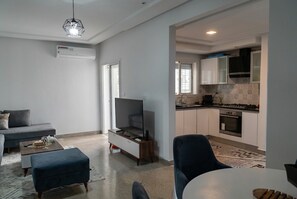 A modern living room with a sofa, ottoman, and a flat-screen TV. - sandra 27 (Tunis)