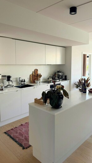 Eine moderne Küche mit weißen Schränken, einer zentralen Kochinsel und einer Kaffeemaschine.