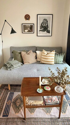 A cozy living room with a grey sofa, patterned cushions, a wooden coffee table with decorative items, and a black floor lamp. - Apartment with two balconies in Copenhagen (København)