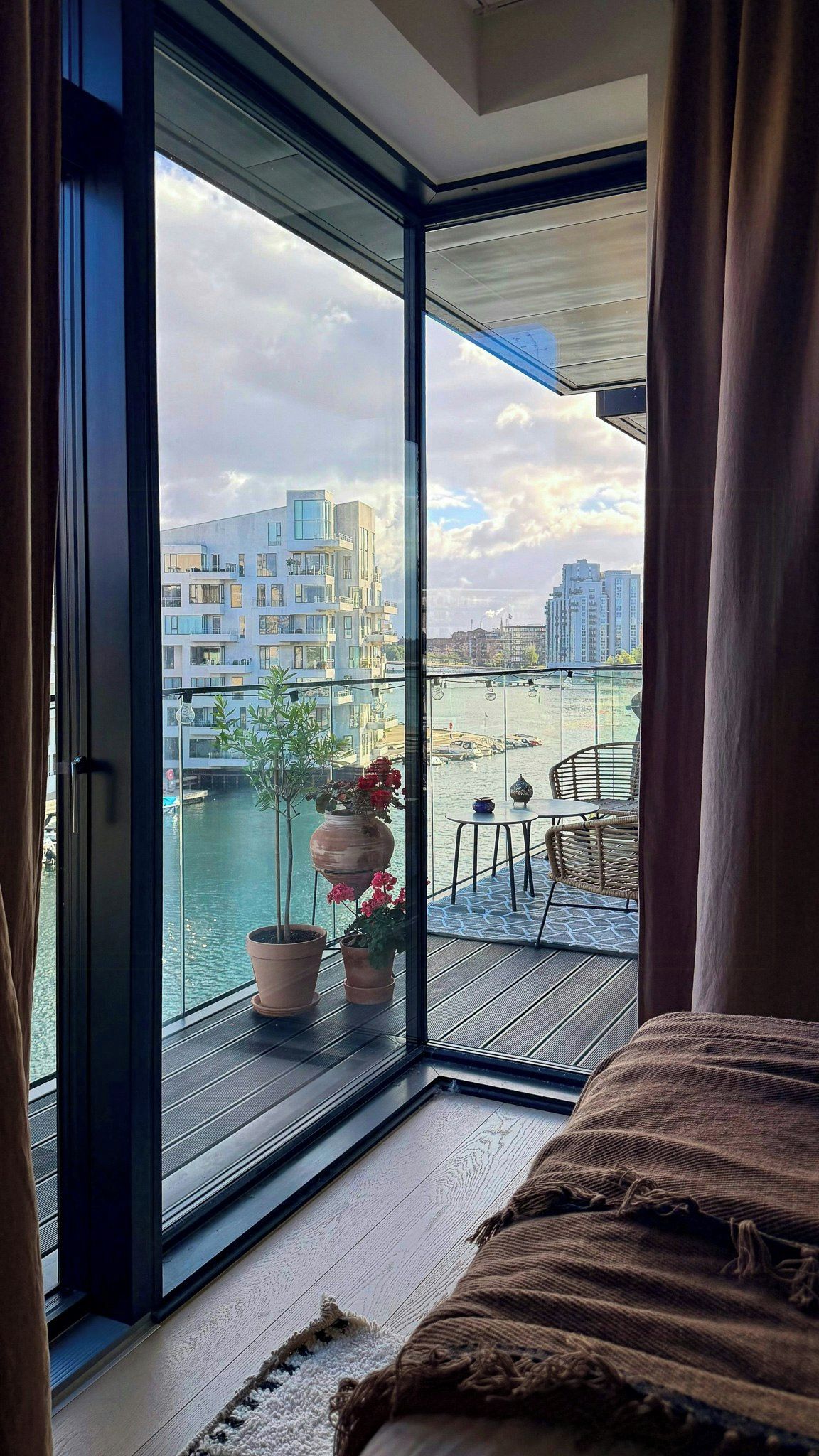 Une pièce dotée d’une grande porte-fenêtre coulissante donnant sur un balcon avec vue sur une rivière et des immeubles.