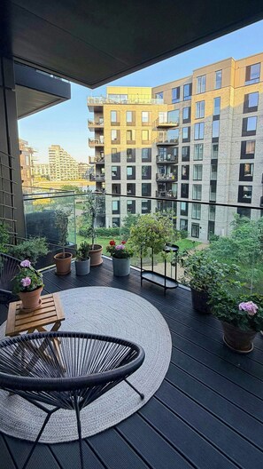 A balcony with a round table and chairs, surrounded by potted plants and overlooking a residential building. - Apartment with two balconies in Copenhagen (København)
