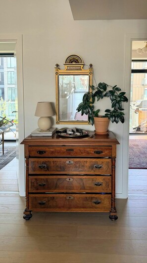 A wooden dresser with multiple drawers, a mirror with an ornate frame, a lamp, and a potted plant. - Apartment with two balconies in Copenhagen (København)