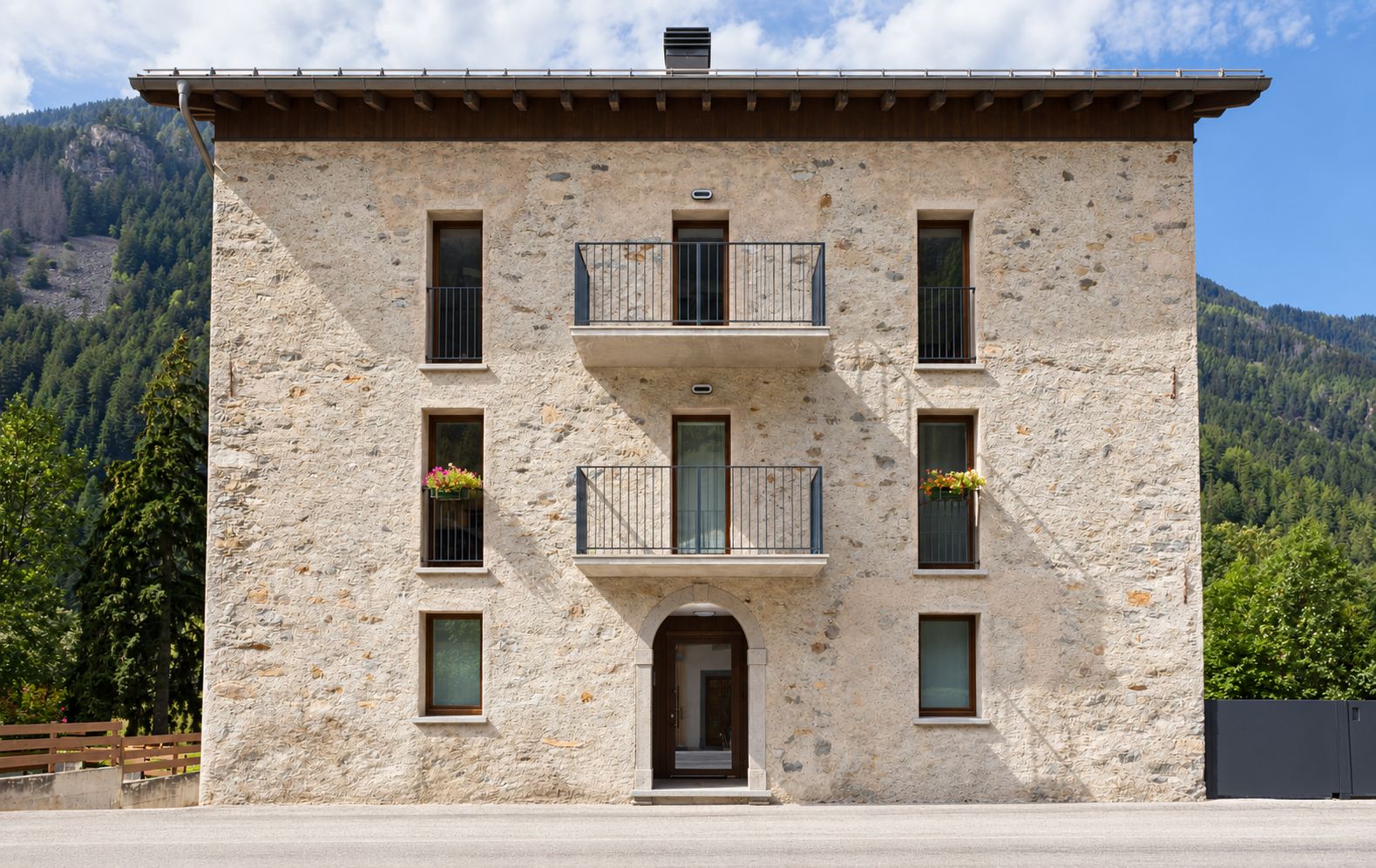 Un bâtiment en pierre avec une entrée centrale, des balcons dotés de garde-corps et des jardinières aux fenêtres.