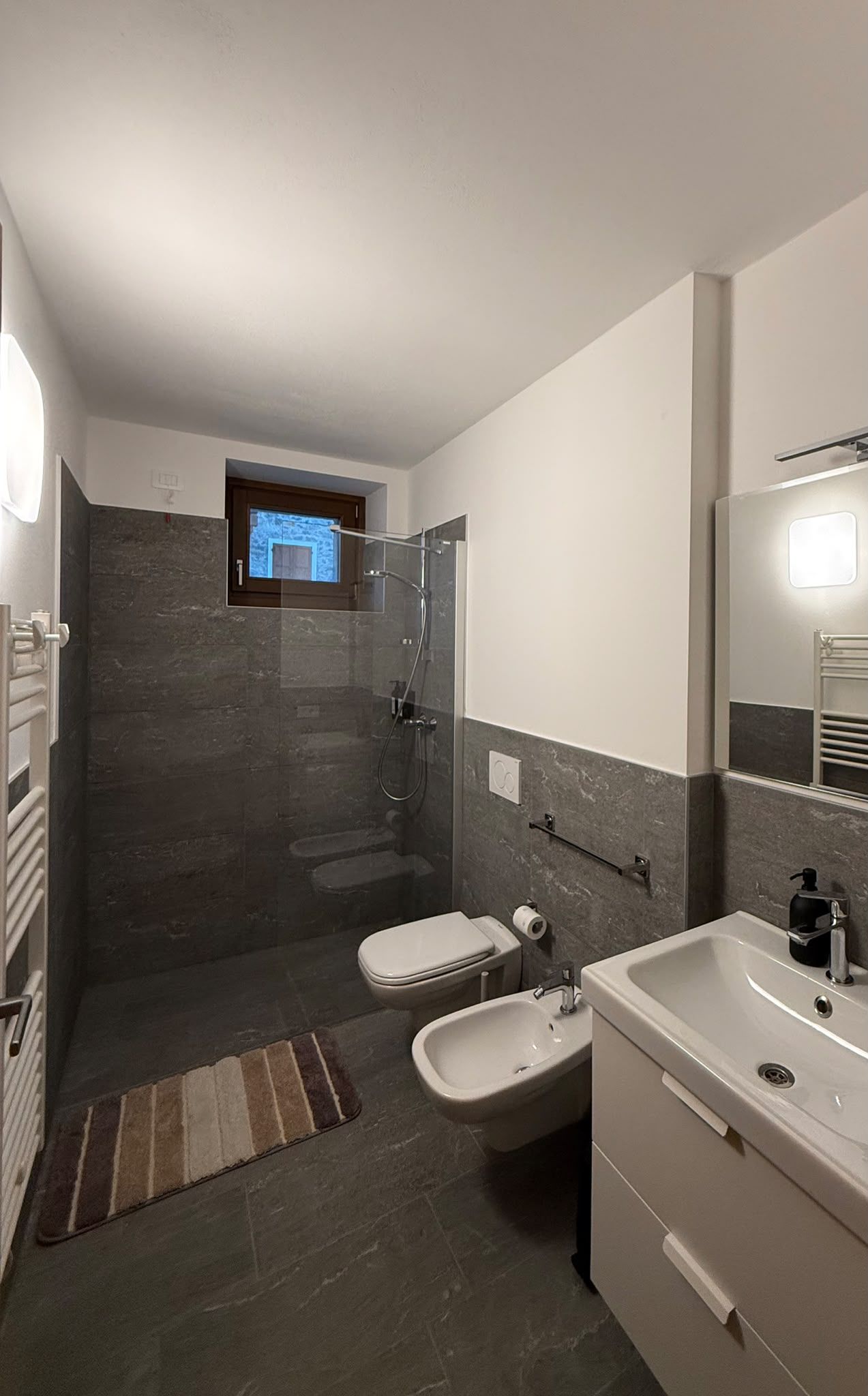 Ein modernes Badezimmer mit einer Duschkabine, einer Toilette, einem Bidet und einem Waschbecken mit Spiegel.