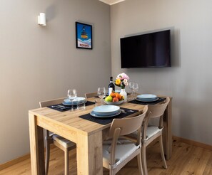 A dining area with a wooden table set for four, a flat-screen TV mounted on the wall, and a framed picture above the table. - Vrbo Property (Cepina)