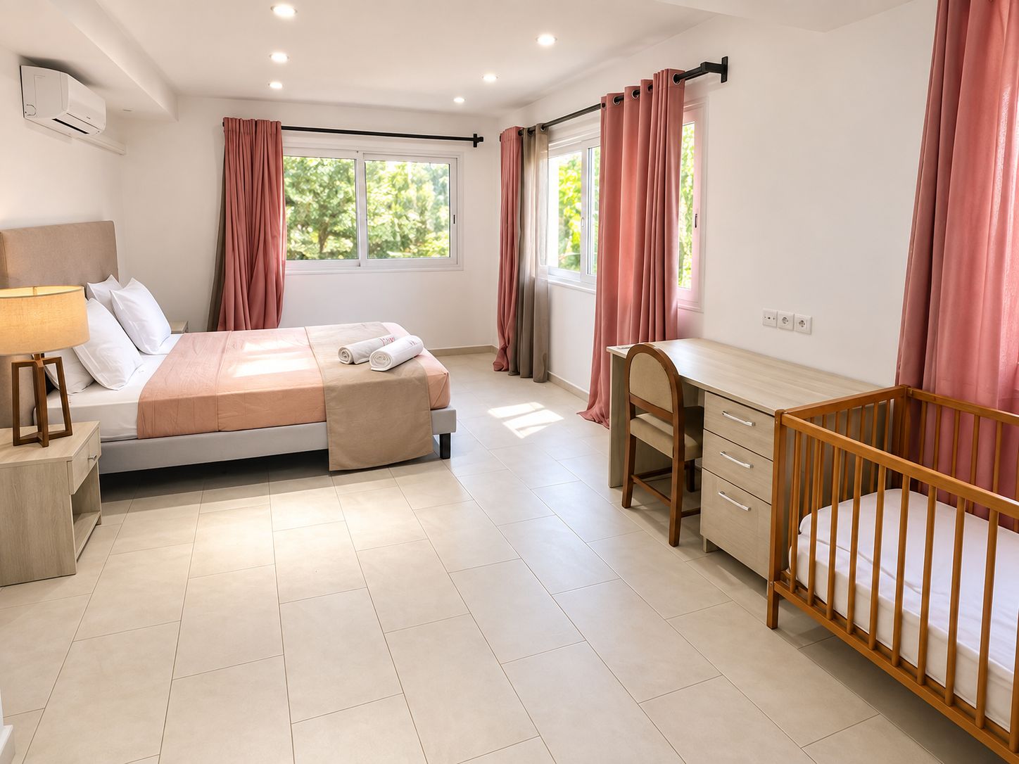 A bedroom with a bed, bedside table, lamp, desk, chair, and crib.