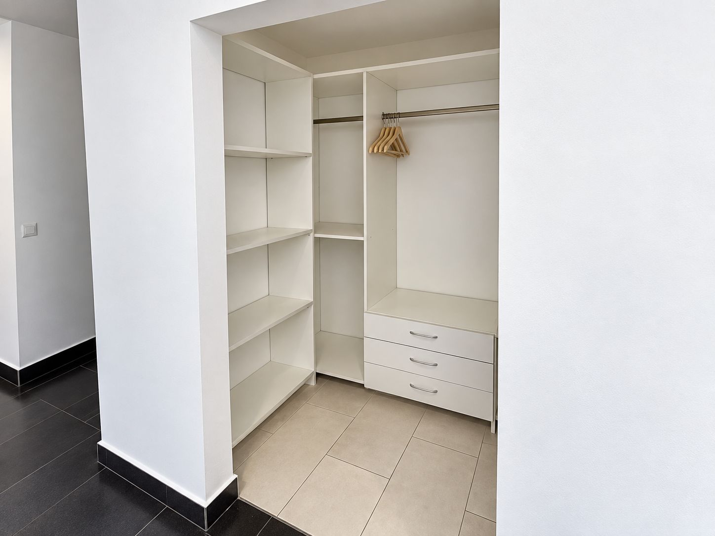 A walk-in closet with open shelving, a hanging rod, and two drawers.