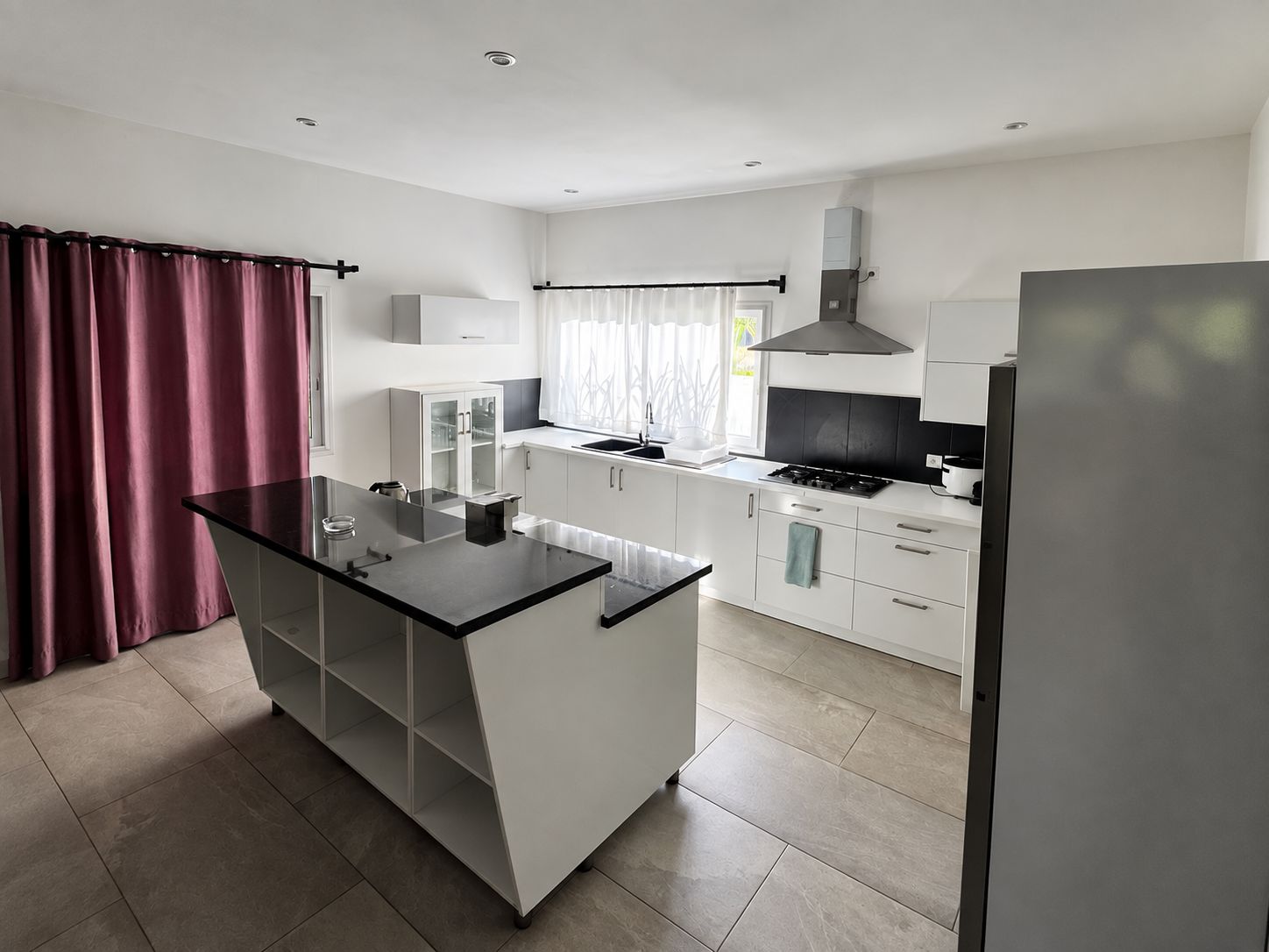 A modern kitchen with a central island, white cabinetry, and a stainless steel refrigerator.