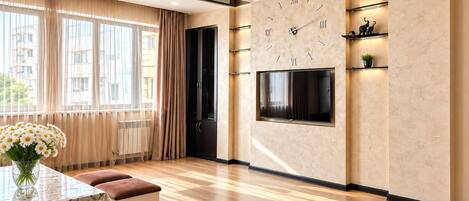 A modern living room with a large wall-mounted TV, a dining area with a table and bench, and a large window with curtains.