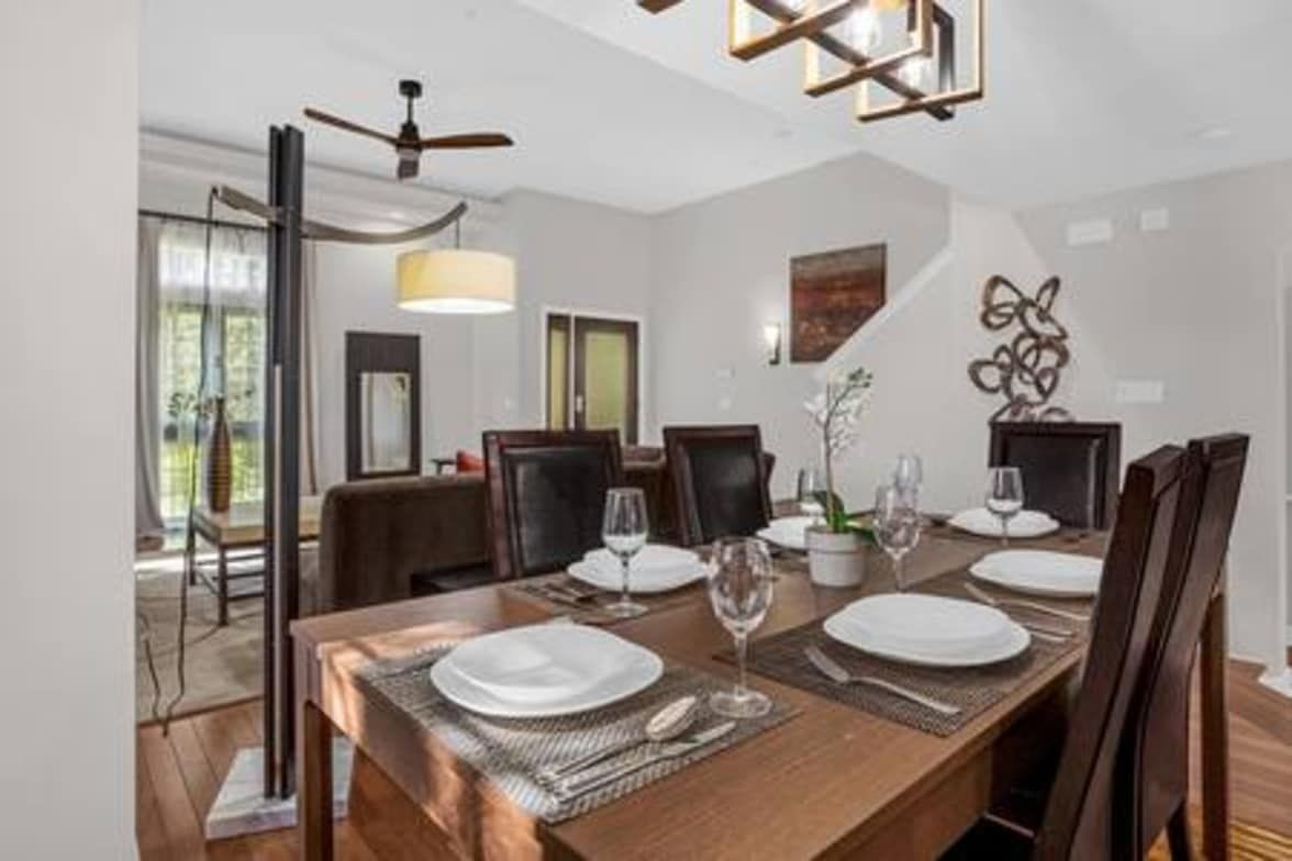 Een eethoek met een lange tafel voor vier personen, omringd door stoelen, met een plafondventilator en hanglampen erboven.