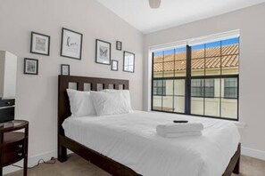 Un dormitorio con cama, mesita de noche, ventana con vista a edificios y cuadros en la pared.