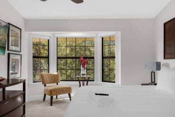 A bedroom with a large bed, a chair, a desk, and a window with a view of trees. - Disney Area Townhome With Resort Pool and Games (Orlando)