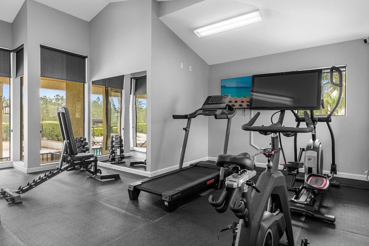 Een sportschool met cardioapparatuur, gewichten en een televisiescherm.