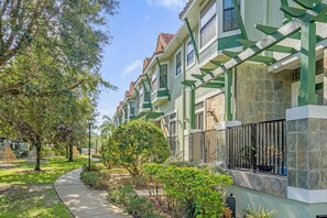 Fileira de casas urbanas com fachada verde e branca, revestimento em pedra e um caminho ladeado por árvores e arbustos.