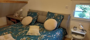 Une chambre à coucher avec un lit, des oreillers, une table de chevet avec une lampe et une fenêtre.