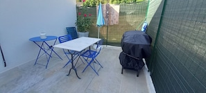 Une terrasse avec une table et des chaises, un barbecue et une clôture verte.