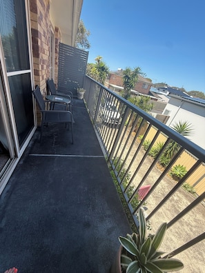 A balcony with a metal railing, a table, two chairs, and potted plants. - 3 bedroom apartment in Evans Head close to shops clubs and beaches. (Evans Head)