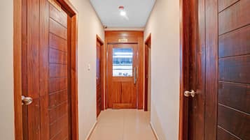 A hallway with wooden doors, a ceiling light, and a view into a room with a window.