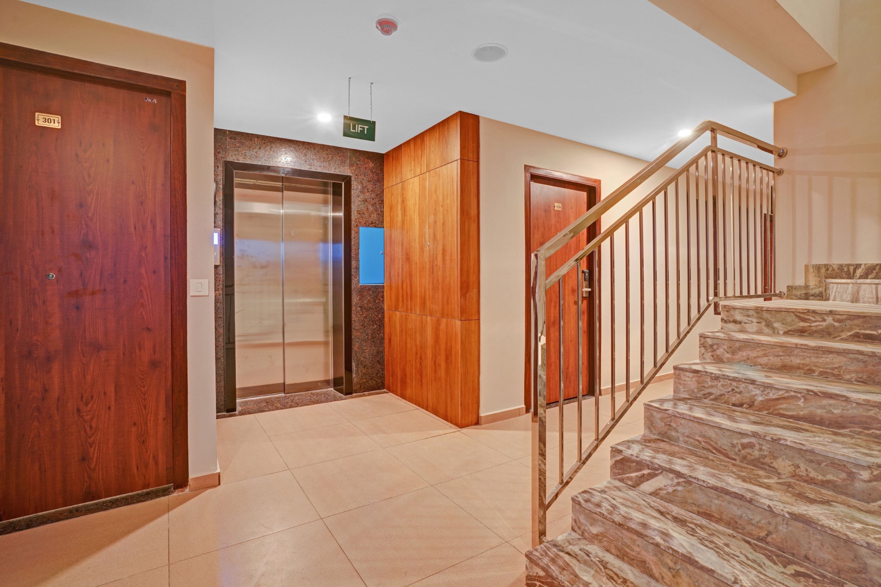 A hotel lobby with a marble staircase, a lift, and wooden doors.