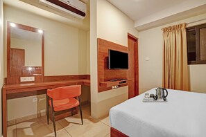 Habitación de hotel con cama, escritorio con silla, televisor montado en la pared y ventana con cortinas.