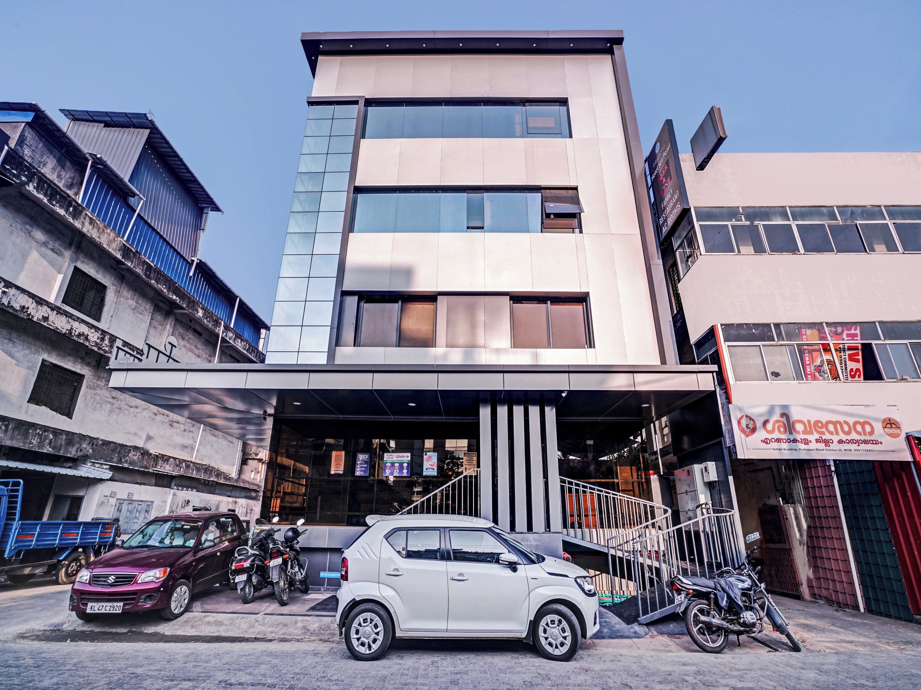 Un bâtiment moderne doté d’une façade en verre, d’une entrée couverte et d’une enseigne indiquant la présence d’un restaurant.