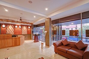 Eine Hotelhalle mit einer Rezeption, einem Ledersofa und einem großen Fenster mit Blick ins Freie.