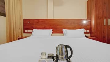 A hotel room with a large bed, wooden headboard, white bedding, and a tray with a kettle and cups.