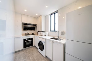 A modern kitchen with white cabinetry, a built-in oven, a microwave, a washing machine, and a refrigerator. - Book&Bed-People's Square Jin'ou Wanguo (Huangpu District,)