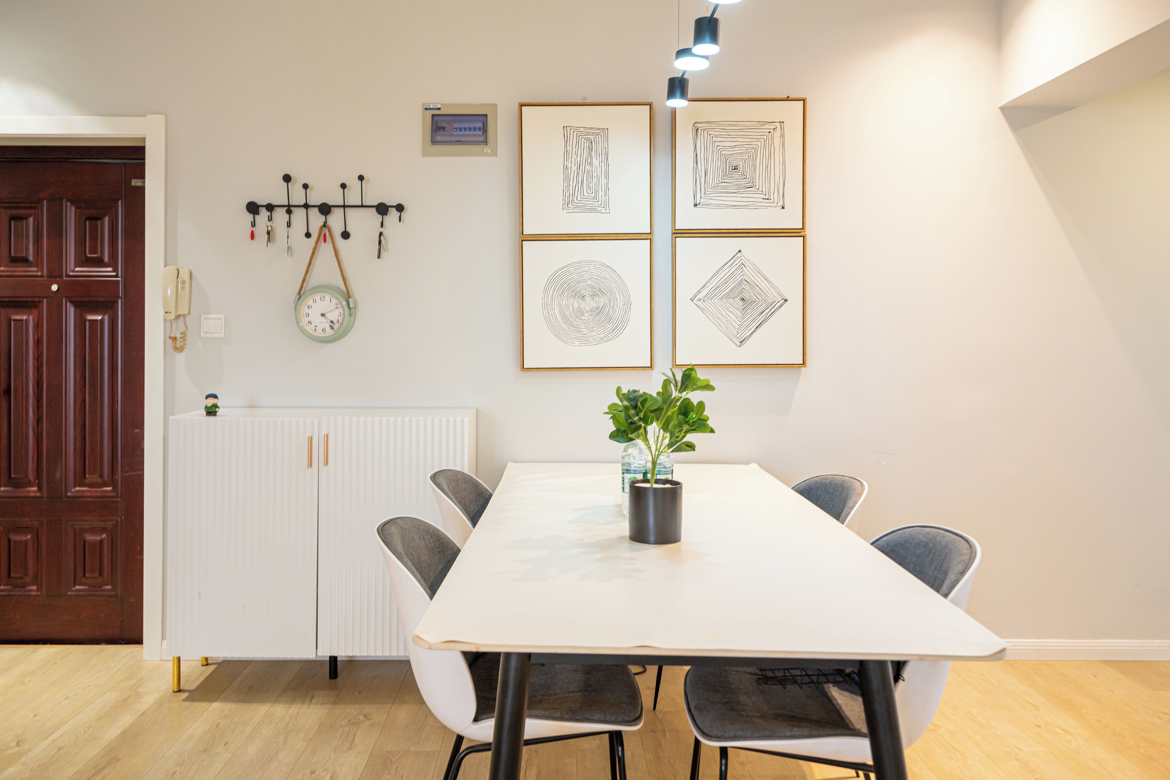 Un comedor con una mesa blanca, cuatro sillas, una planta en maceta y cuadros en la pared.