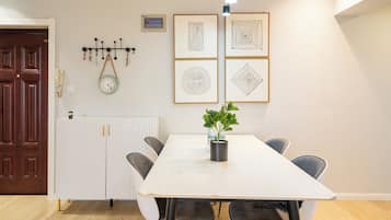 Un comedor con una mesa blanca, cuatro sillas, una planta en maceta y cuadros en la pared.