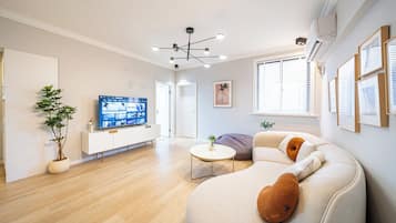 Een moderne woonkamer met een bank, een salontafel, een televisie op een kast en een plant in een pot.