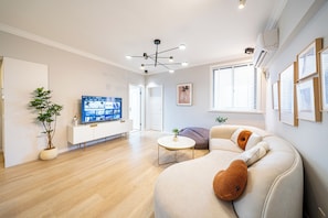A modern living room with a sofa, a coffee table, a TV on a cabinet, and a potted plant. - Book&Bed-People's Square Jin'ou Wanguo (Huangpu District,)