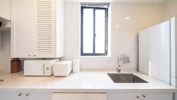 Una cocina moderna con armarios blancos, microondas integrado, un lavamanos y una ventana con persianas.